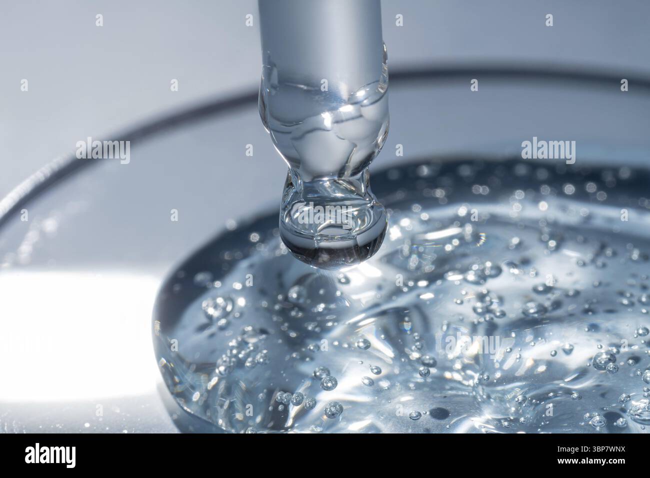 Primo piano della pipetta con il versamento di gel di siero liquido e ombre su sfondo blu. Cosmetici alla moda con ombre dure Foto Stock