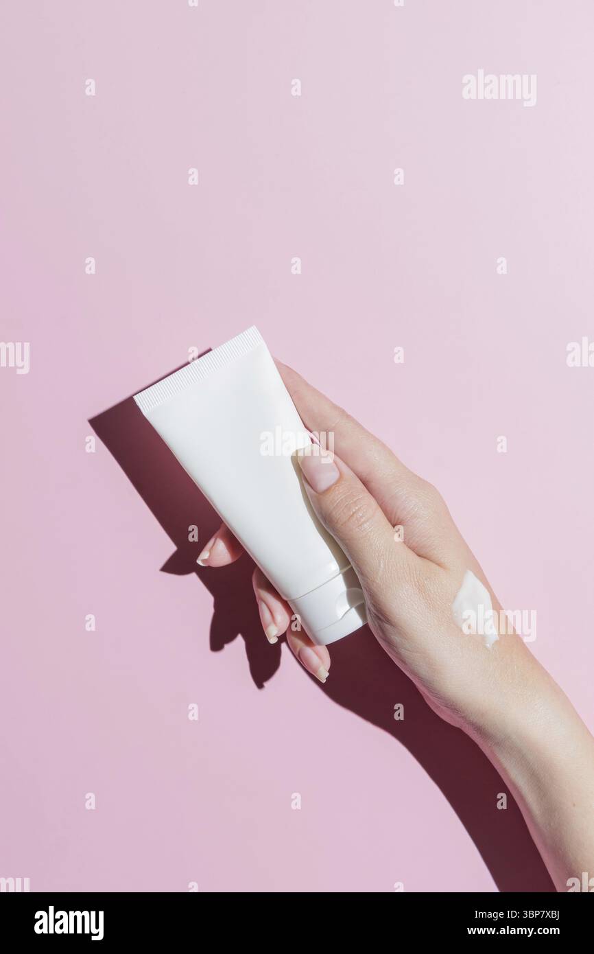 Mano di donna con un tubo e un campione di crema su sfondo rosa. Concetto di prodotti cosmetici. Copia spazio. Ombre dure Foto Stock