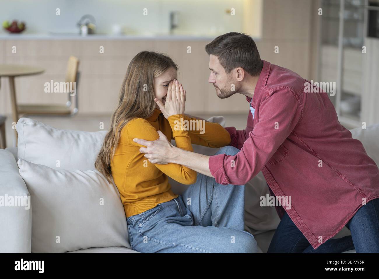 Il marito tiranno grida e scuote la moglie piangendo, litigando e afferrando le mani sul divano. Lite familiare, violenza domestica e impossibilità di escapi Foto Stock