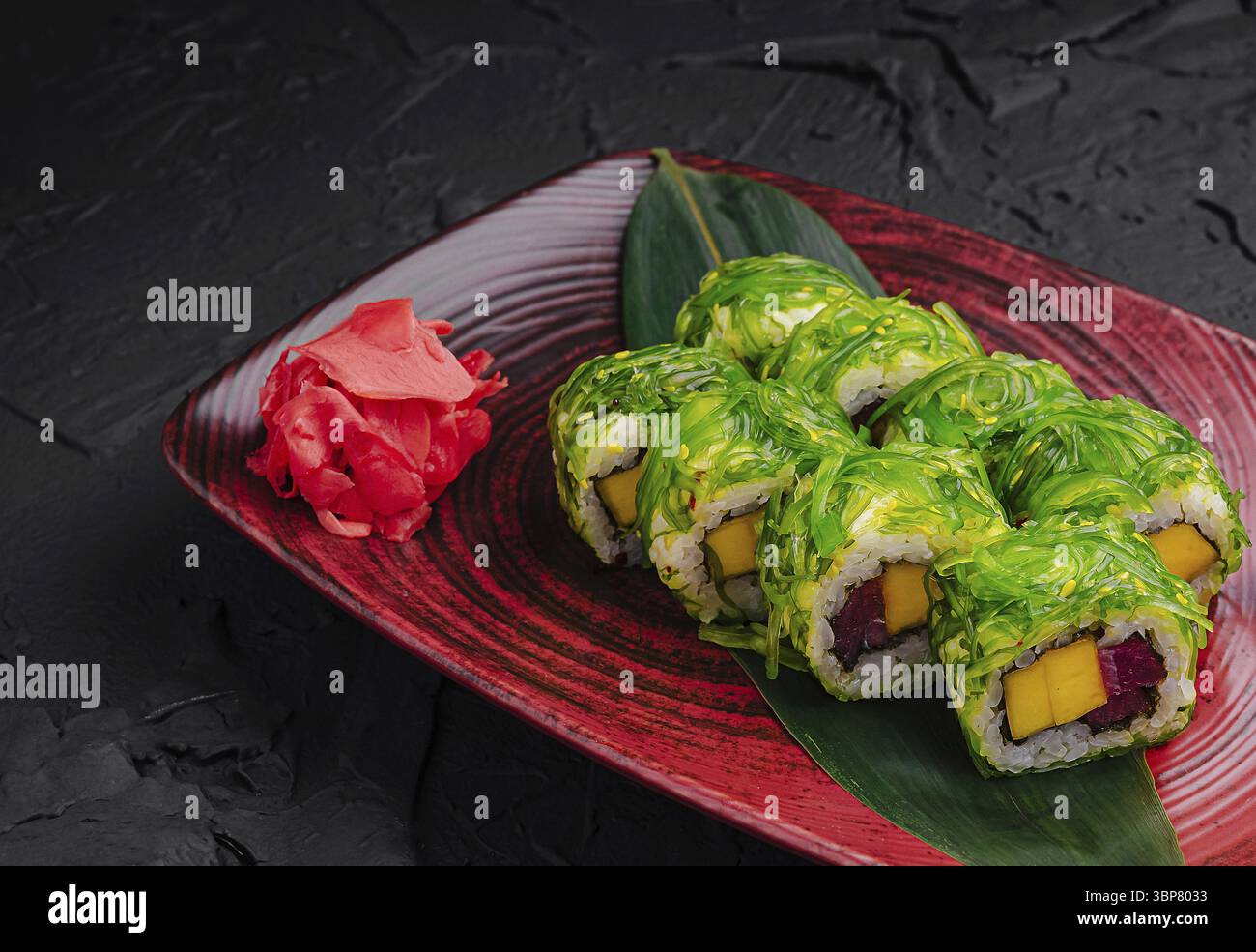 Cibo, coloratissimi sushi roll sono disposti su un piatto rosso vivace. Questi panini sono avvolti in alghe verdi fresche con ripieni di mango e pesce. Un lato Foto Stock