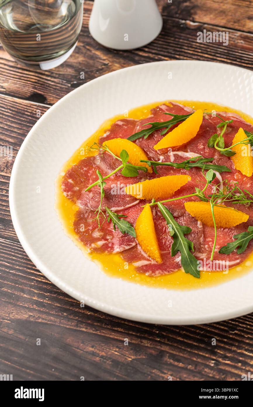 Carpaccio di manzo a fette sottili con segmenti di arancia e foglie di rucola Foto Stock