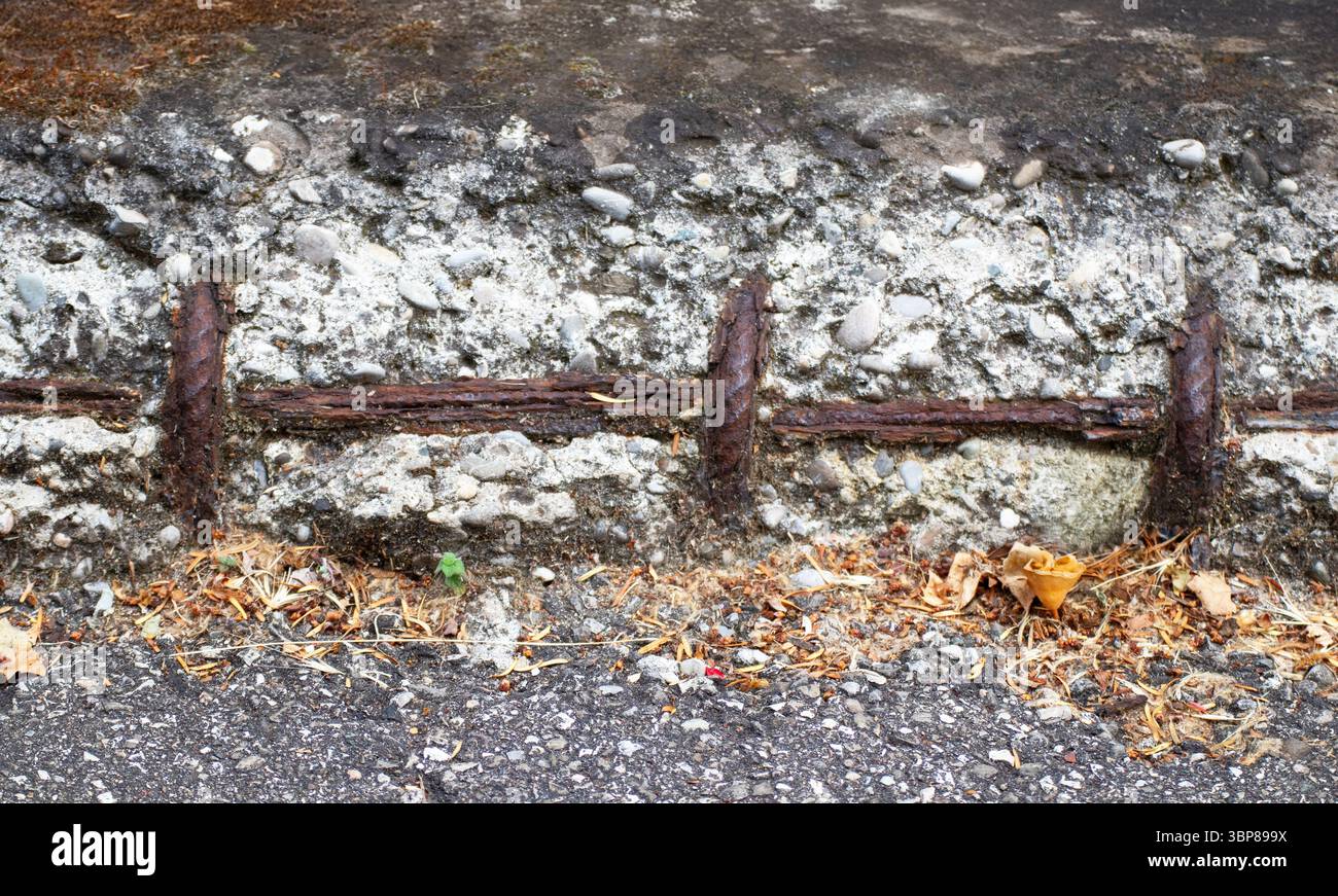 Armatura arrugginita esposta in calcestruzzo sbriciolato mostra il decadimento urbano texture grintose deterioramento industriale infrastruttura rotta dettagli grezzi. Foto Stock