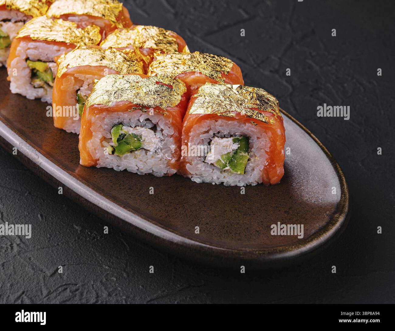 Cibo, eleganti sushi con foglie dorate, serviti su un piatto di ceramica su uno sfondo scuro Foto Stock