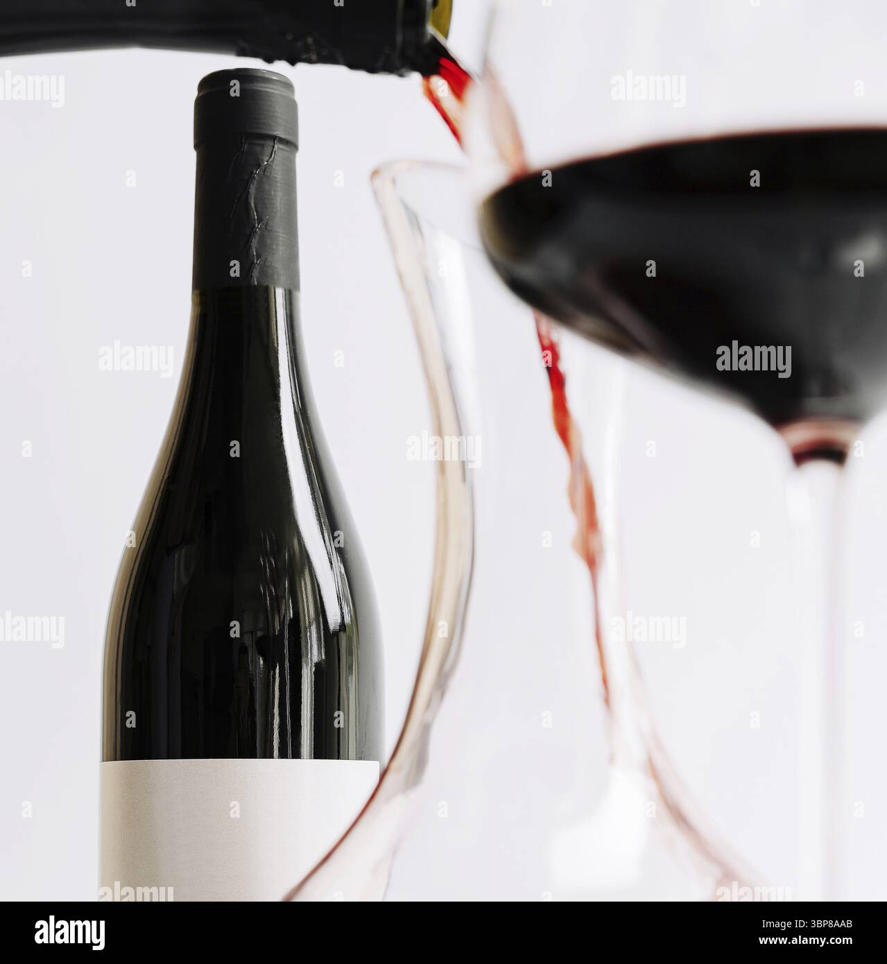 Cibo, Una bottiglia di vino rosso viene posizionata su un tavolo mentre il vino viene versato in un bicchiere. L'impostazione è minimalista e mette in evidenza i colori intensi Foto Stock