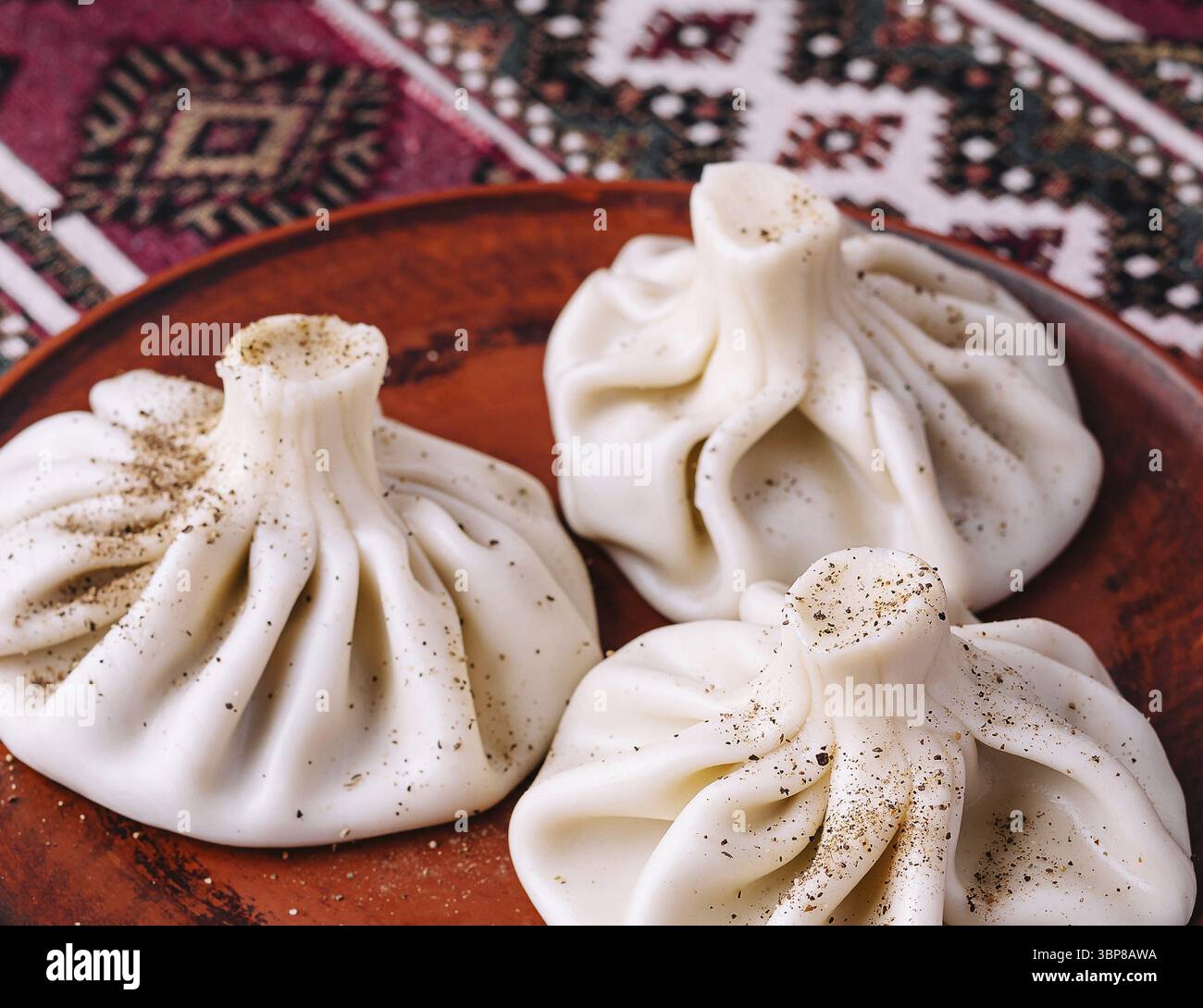 Cibo, tre gnocchi di khinkali georgiani serviti su un piatto di argilla su una tovaglia a motivi etnici Foto Stock