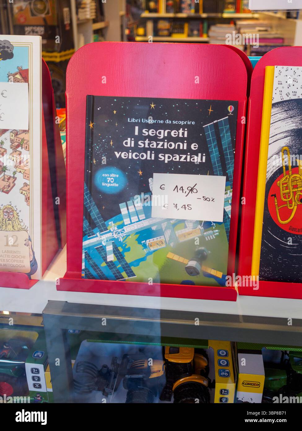 Cremona, Italia 28 giugno 2025 Libreria vetrina con i segreti di stazioni e veicoli spaziali, un libro per bambini di Usborne Publishing, a fianco di c Foto Stock