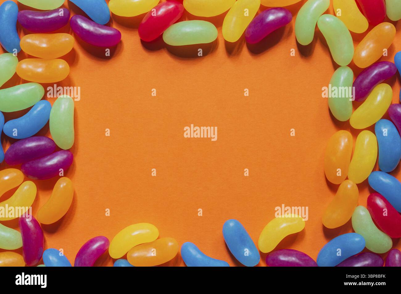 Jelly Beans assortiti bordo con copyspace su sfondo arancione Foto Stock
