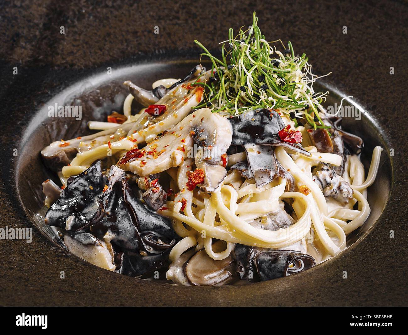 Cibo, noodles gourmet fritti in padella con frutti di mare, guarniti con microgreen, presentati su un elegante piatto scuro Foto Stock