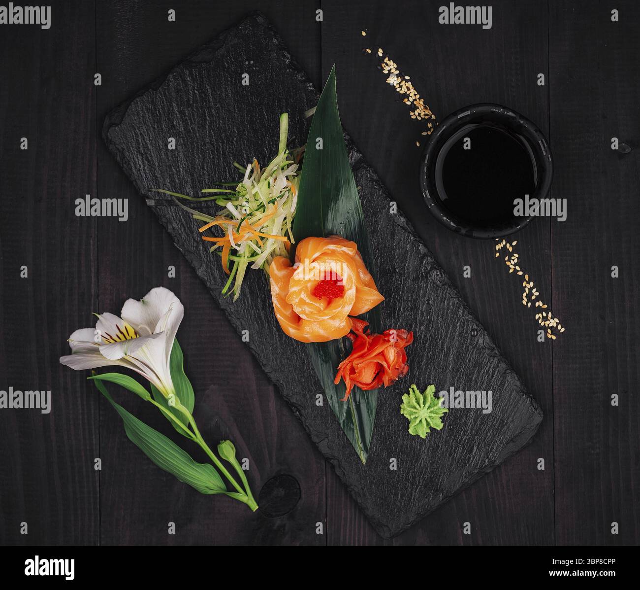Cibo, delizioso antipasto al salmone sashimi servito su ardesia nera con wasabi, zenzero sottaceto, salsa di soia e fiore bianco Foto Stock