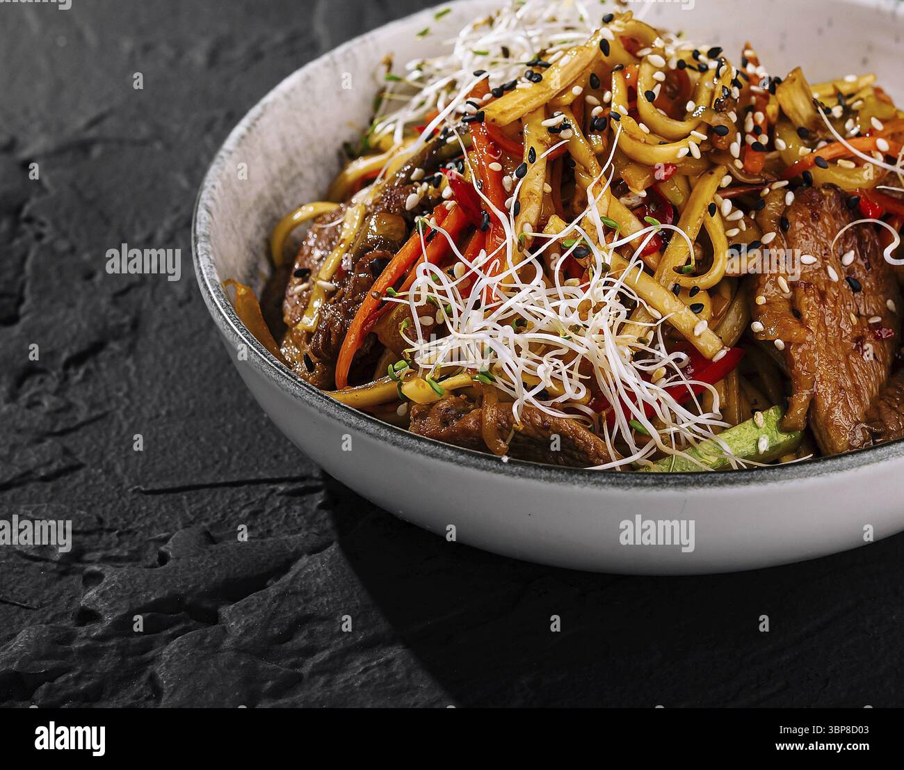 Cibo, manzo saltato in padella con spaghetti, verdure colorate e semi di sesamo in un recipiente Foto Stock