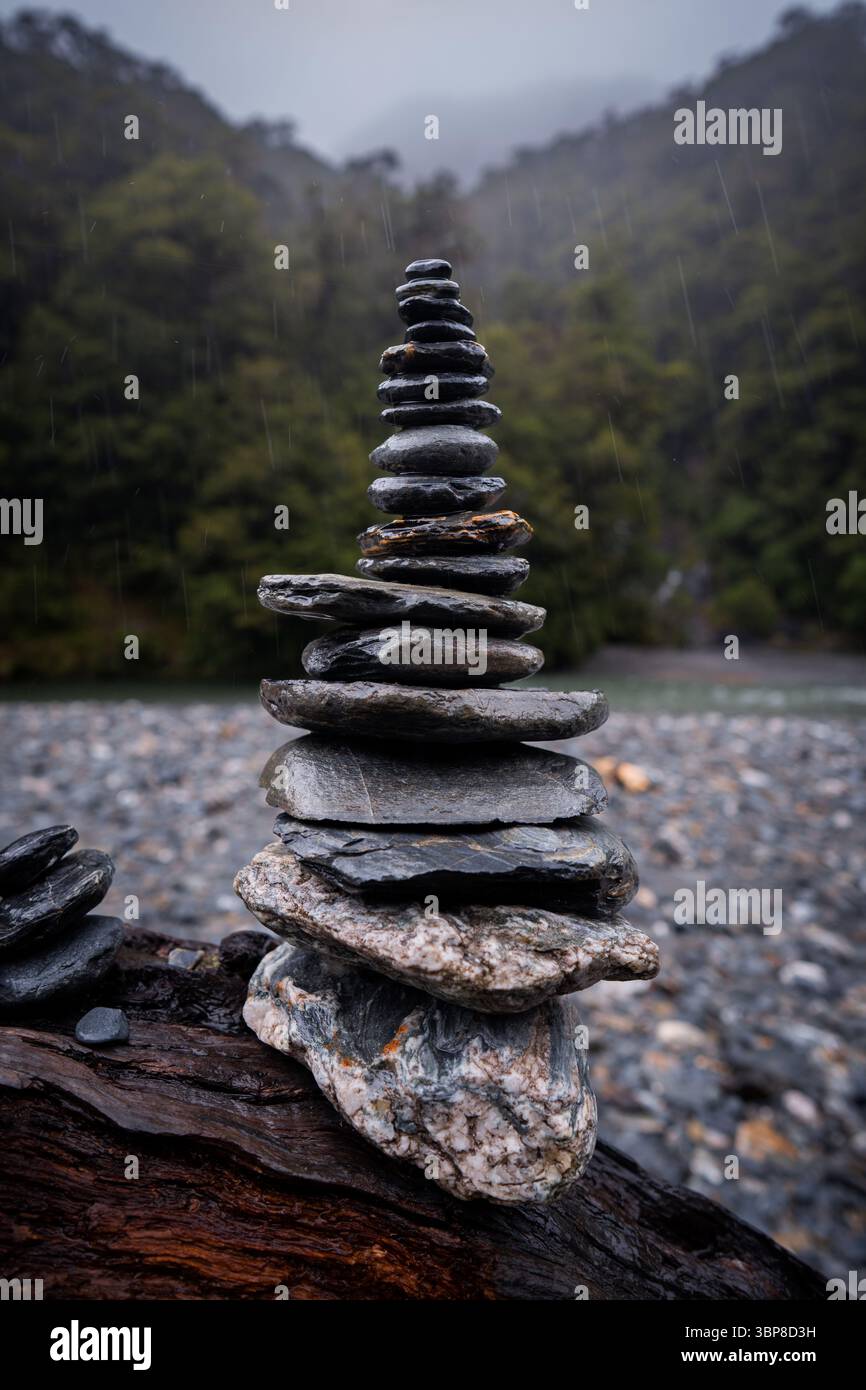 Una torre di pietre piatte, accuratamente impilata, poggia su un terreno boscoso e nebbioso. Le gocce di pioggia aggiungono movimento, evidenziando la pazienza, ba Foto Stock