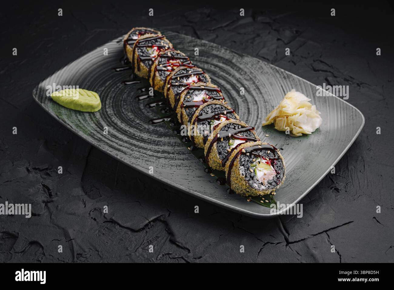 Cibo, Un lungo sushi roll è elegantemente disposto su un piatto scuro. È guarnita con un filo di salsa, wasabi e zenzero sottaceto, showcasin Foto Stock