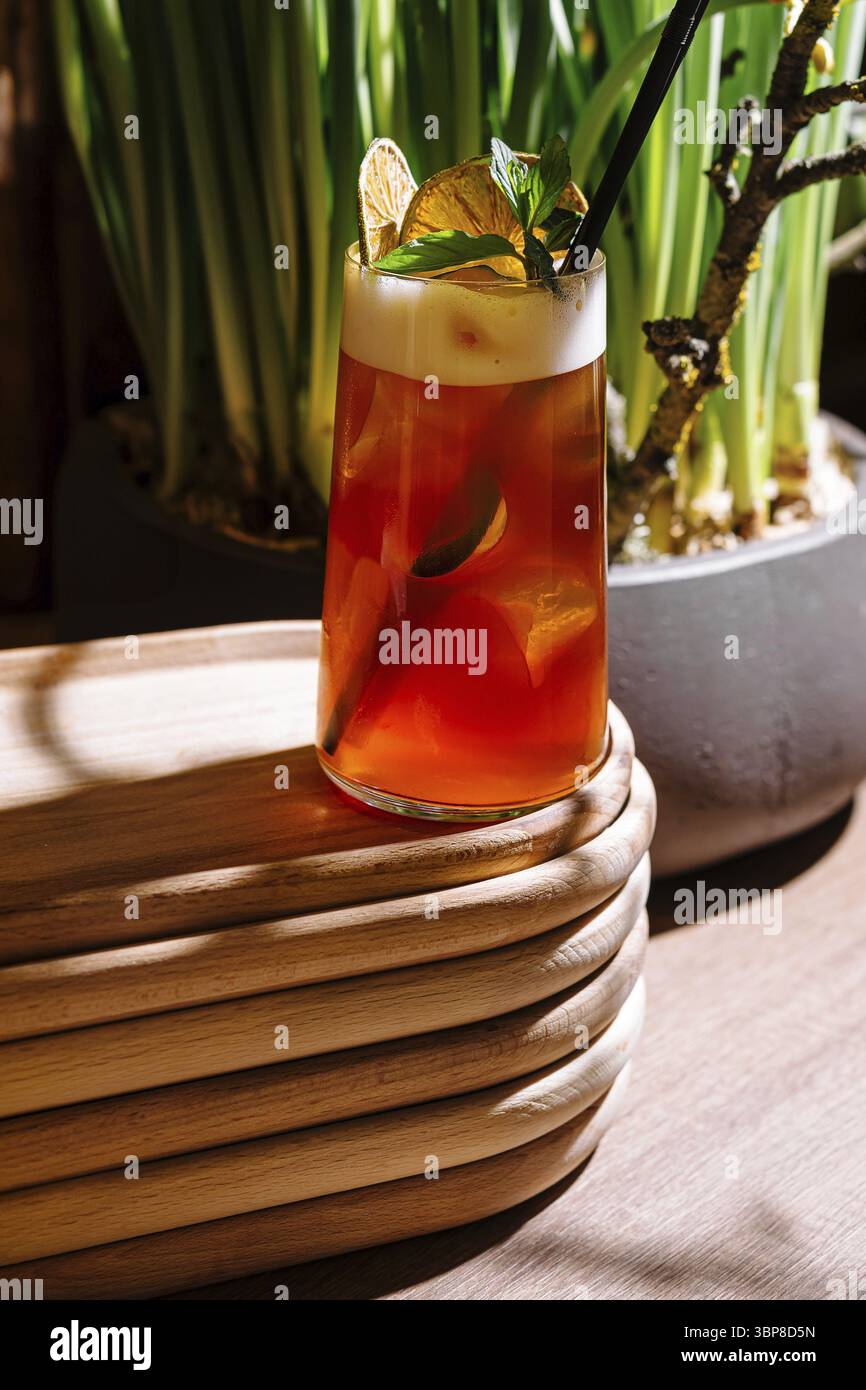 Cibo, rinfrescante cocktail di tè freddo con agrumi e foglie di menta, servito su un elegante vassoio di legno in un moderno caffè Foto Stock