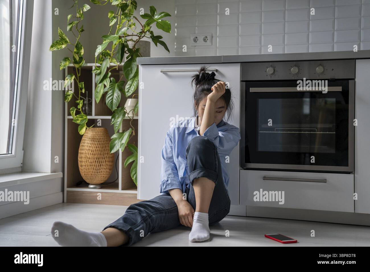La ragazza asiatica turbata si siede sul pavimento vicino al telefono cellulare si sente male sola triste a casa. Infelice donna coreana che soffre di una cattiva relazione rompere ha psy Foto Stock