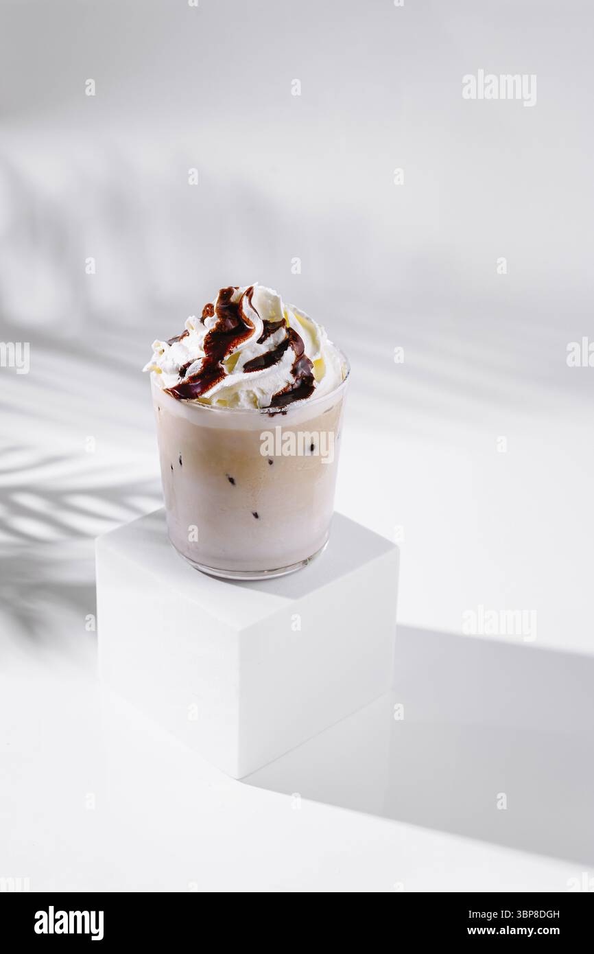 Cibo, caffè ghiacciato rinfrescante con panna montata e salsa al cioccolato, che crea un'ombra fresca su uno sfondo bianco minimalista Foto Stock
