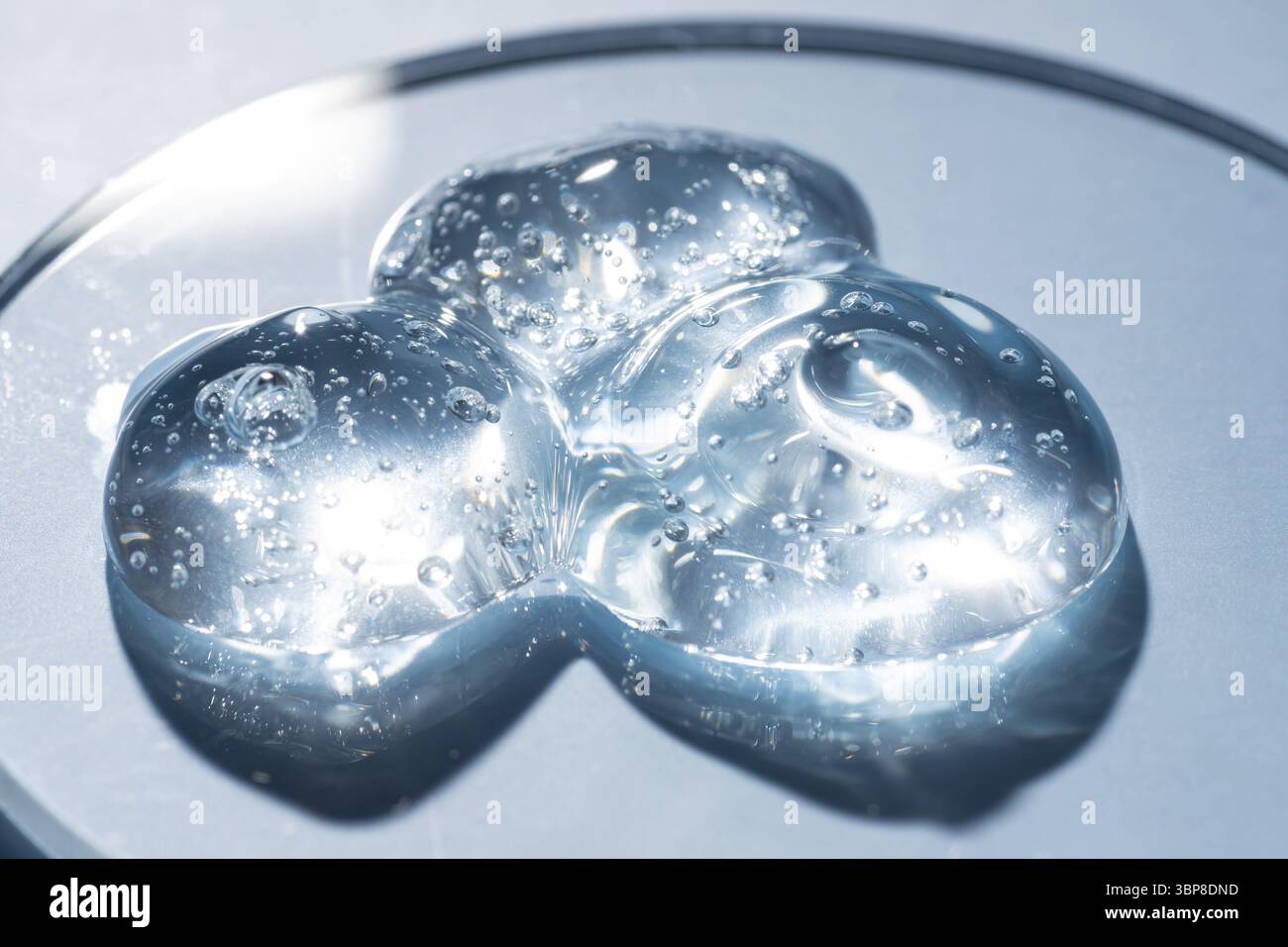 Goccia o sbavatura di cosmetici. Goccia di gel trasparente liquido con bolle su sfondo blu su piastra Petri Foto Stock