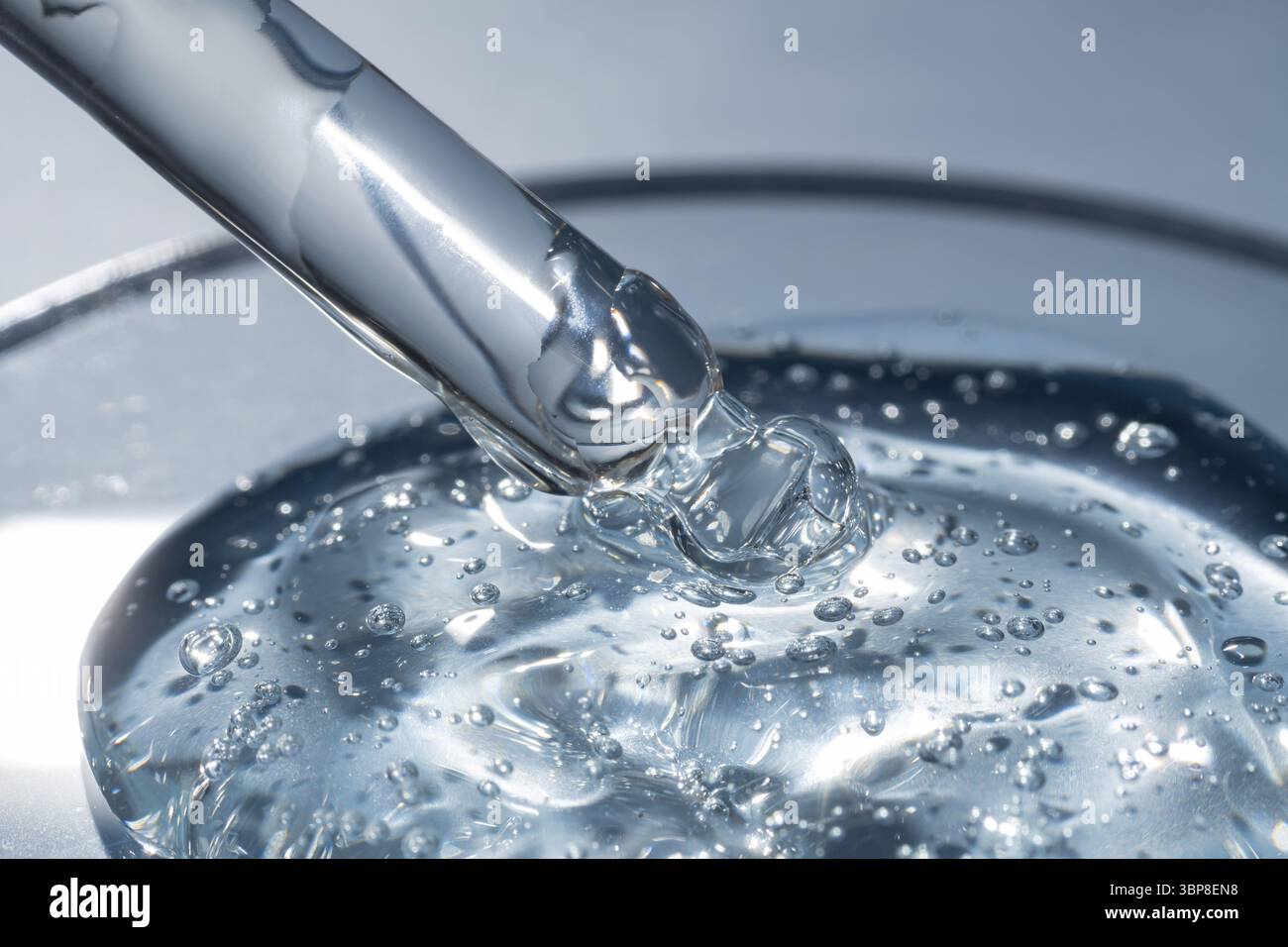 Primo piano della pipetta con il versamento di gel di siero liquido e ombre su sfondo blu. Cosmetici alla moda con ombre dure Foto Stock