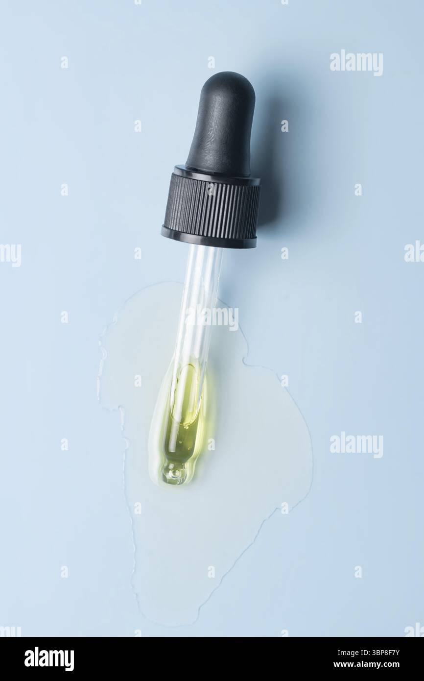 Primo piano della pipetta con il versamento di siero liquido e ombre su sfondo blu. Cosmetici alla moda con ombre dure Foto Stock