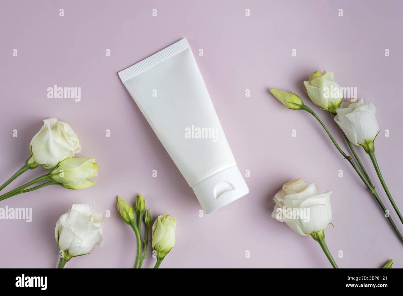 Leere weisse Plastiktube Fuer Creme, Maske, Shampoo oder Zahnpasta auf rosa Hintergrund unter Eustoma Blumen. Fruehling Praesentation von Kosmetik-Pak Foto Stock