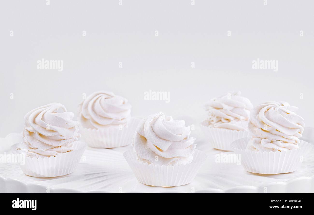 Cibo, cinque cupcake da buongustai con glassa rosa e bianca su un classico piedistallo bianco su uno sfondo senza cuciture Foto Stock