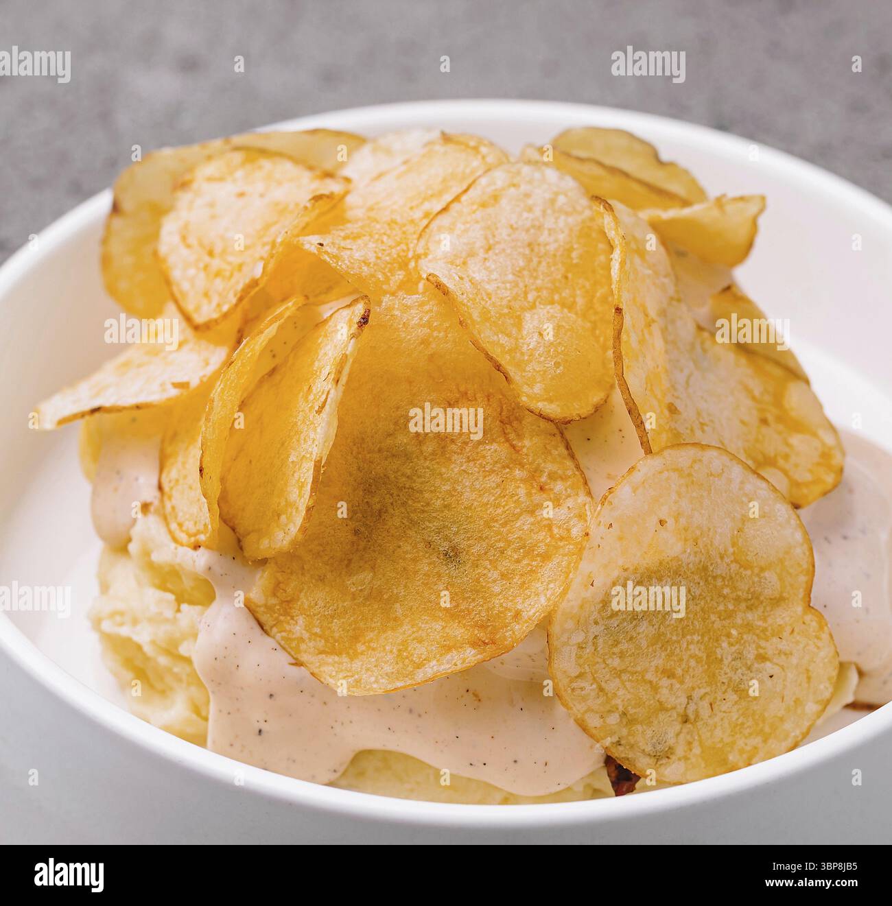 Cibo, patatine appetitose servite in una ciotola bianca su sfondo grigio testurizzato Foto Stock