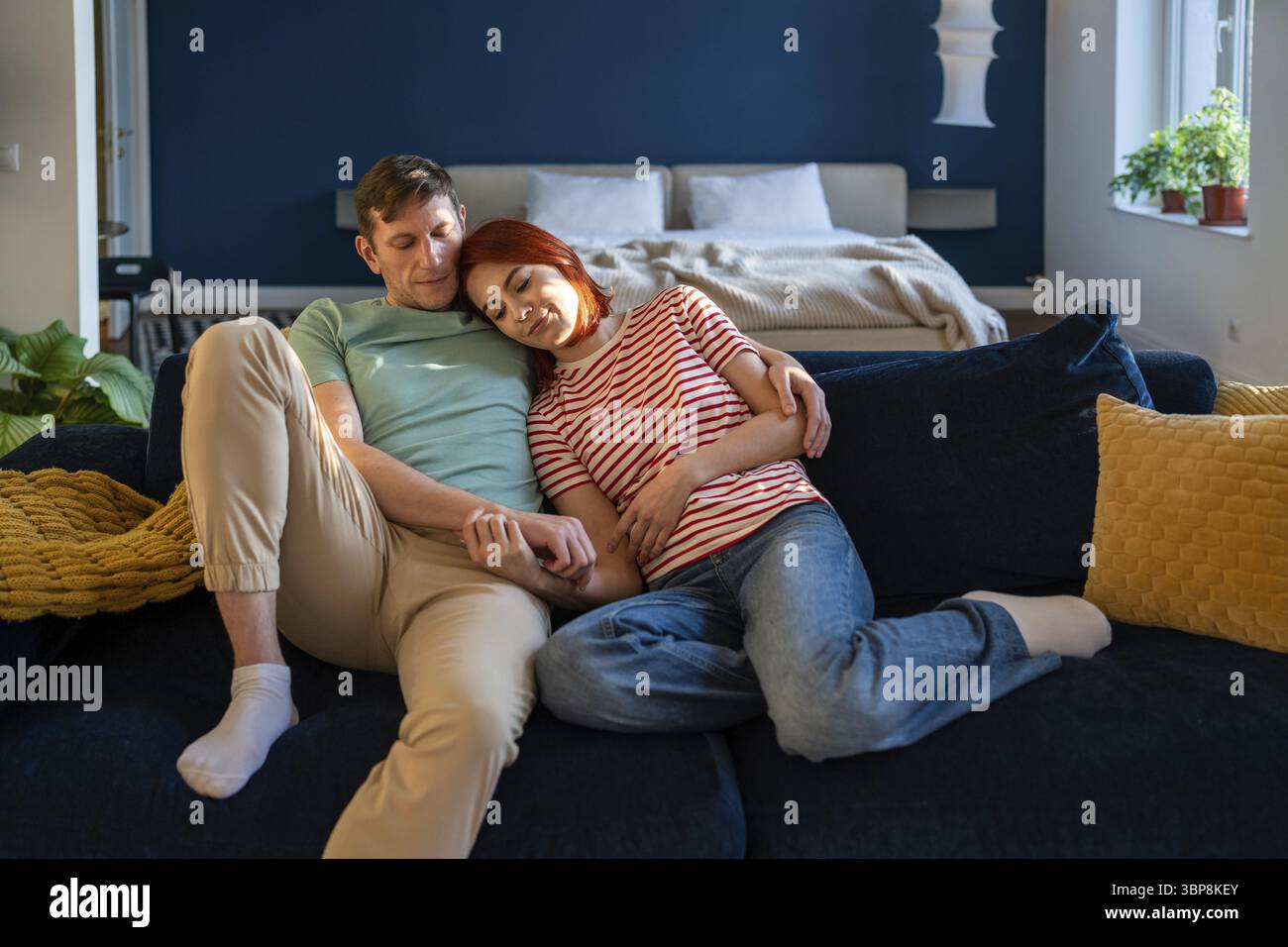 Affettuosa coppia di famiglia di mezza età che abbraccia seduto sul divano a casa tenendosi per mano. Donna rilassata che giace sulla spalla dell'uomo a occhi chiusi. Amorevole Foto Stock
