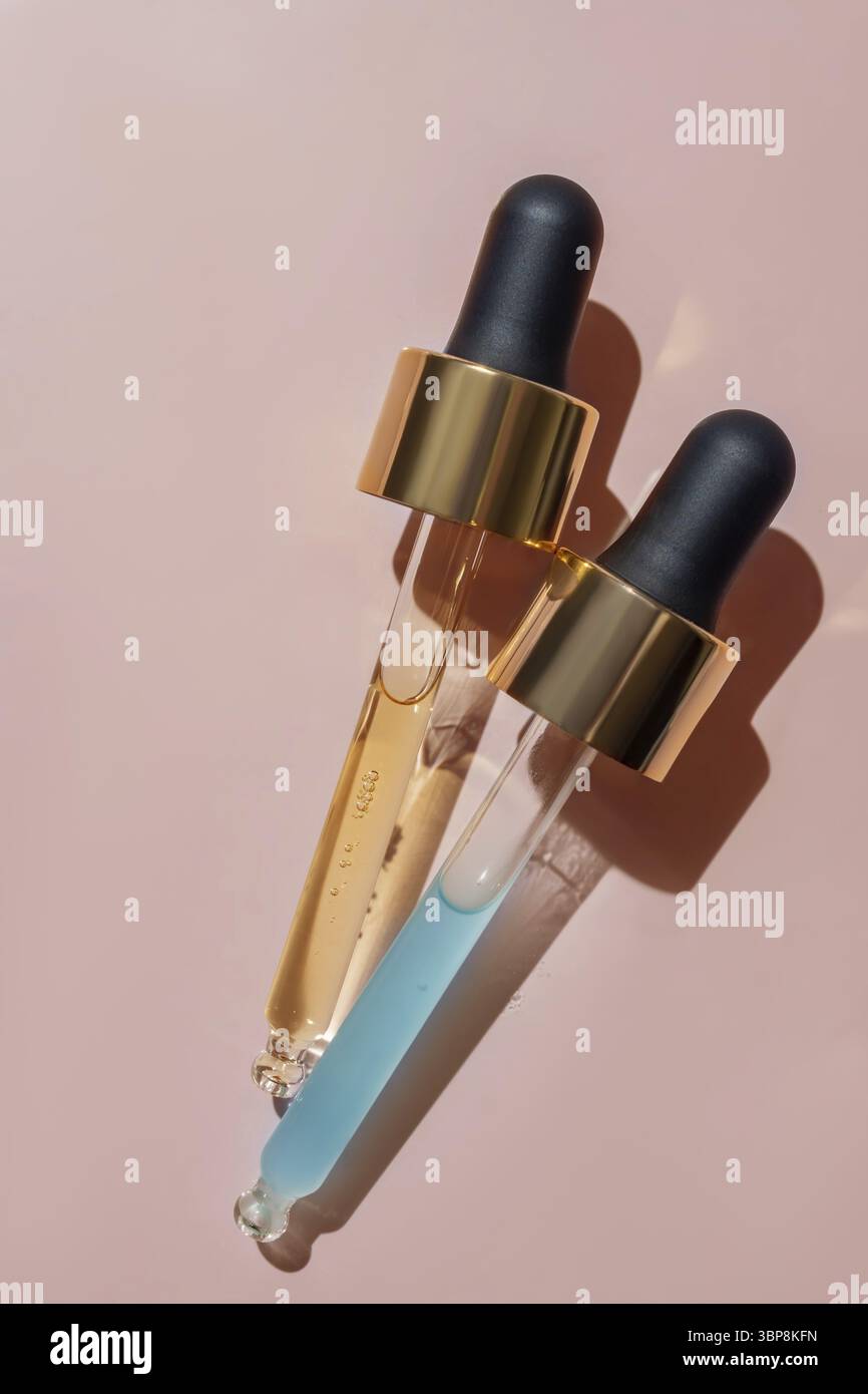 Primo piano di due pipette con versamento di siero liquido e ombre sullo sfondo beige. Cosmetici alla moda con ombre dure Foto Stock