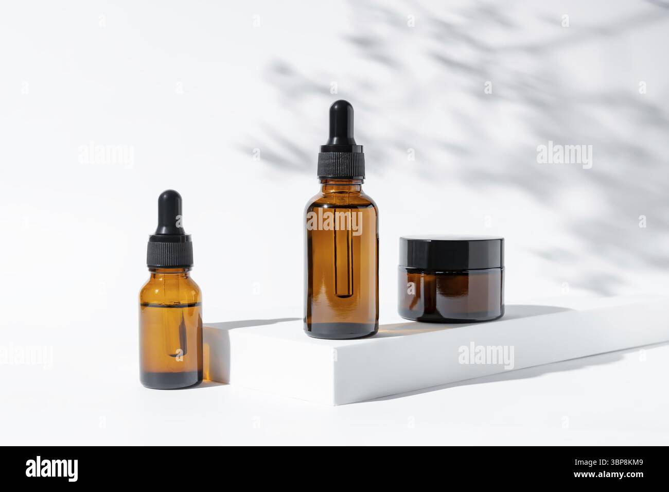 Cosmetici naturali in vetro ambrato su sfondo bianco con ombre floreali. Set di prodotti di bellezza biologici per il CENTRO BENESSERE. Concetto di cura della pelle Foto Stock