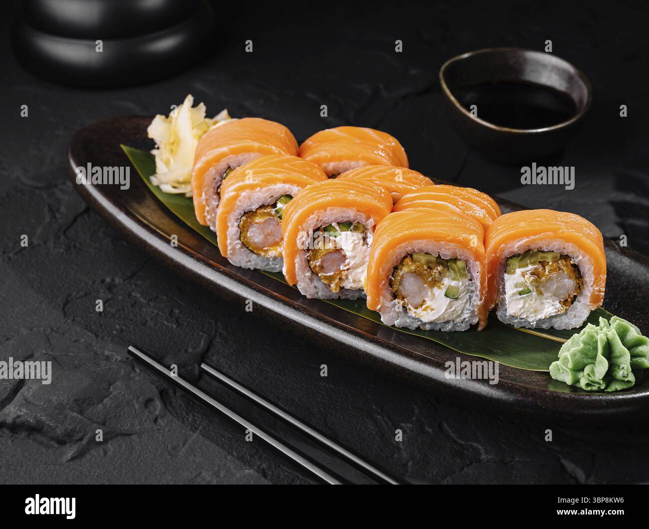 Cibo, delizioso sushi di salmone servito su un elegante piatto scuro con salsa di soia, perfetto per i temi della cucina asiatica Foto Stock
