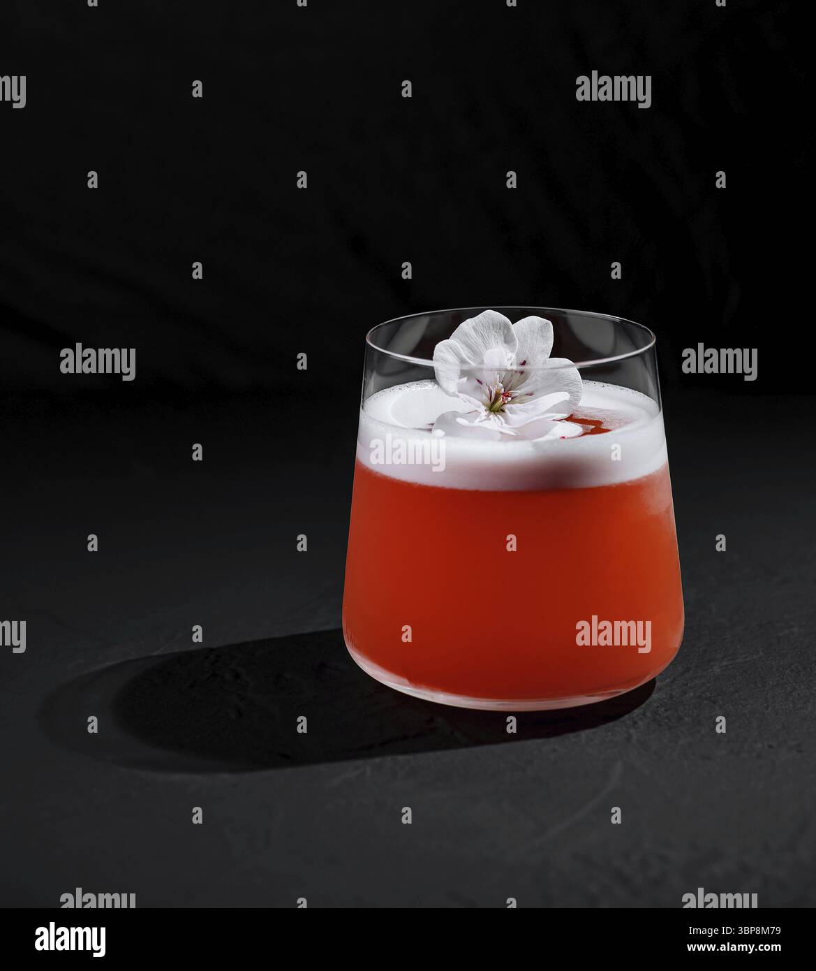 Cibo, cocktail sofisticato adornato da una decorazione floreale bianca su uno sfondo scuro Foto Stock