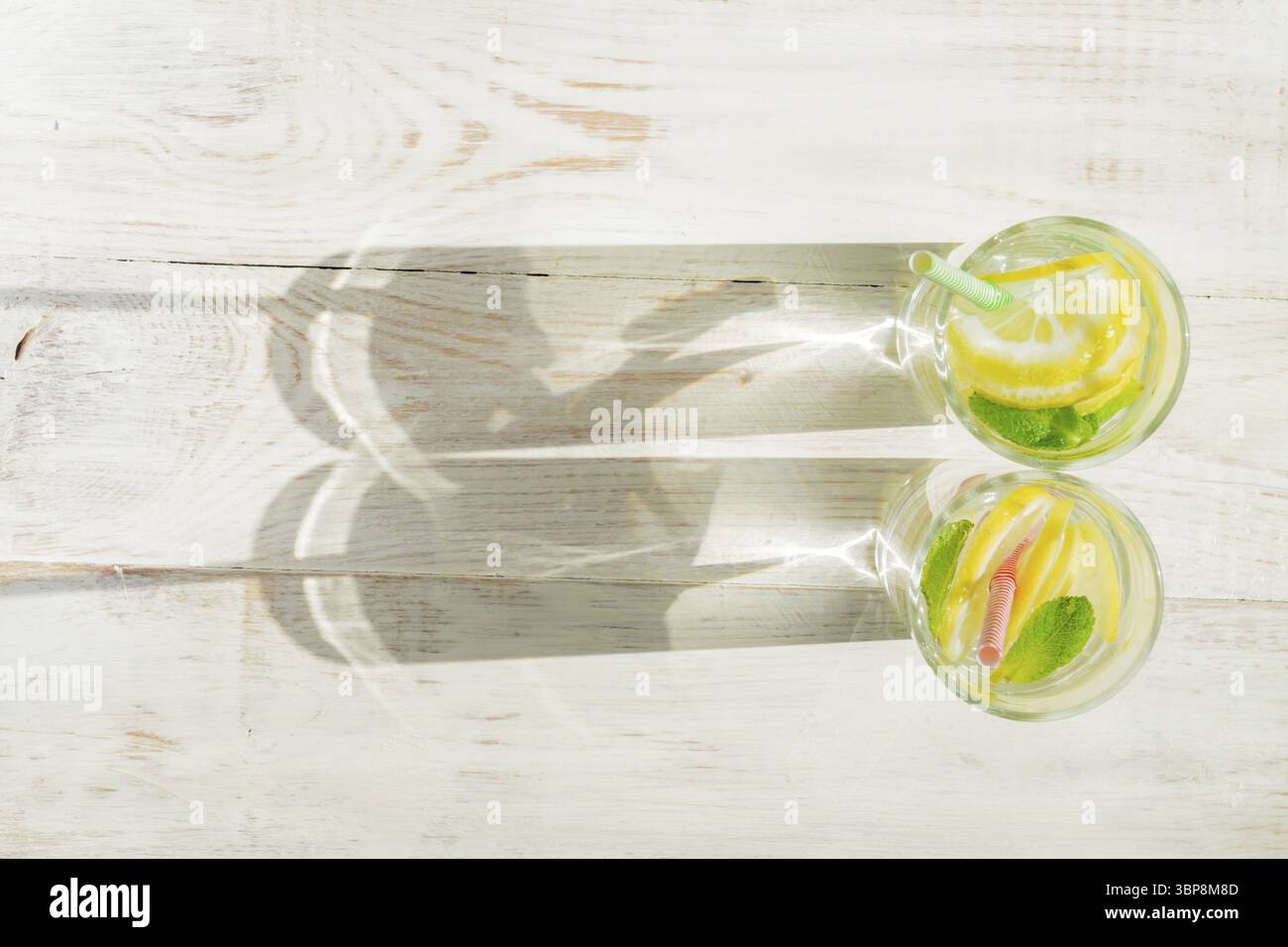 Bicchiere di limonata fatta in casa con limoni, menta e cannucce di carta su fondo rustico in legno. Bevanda rinfrescante estiva. ombre dure Foto Stock