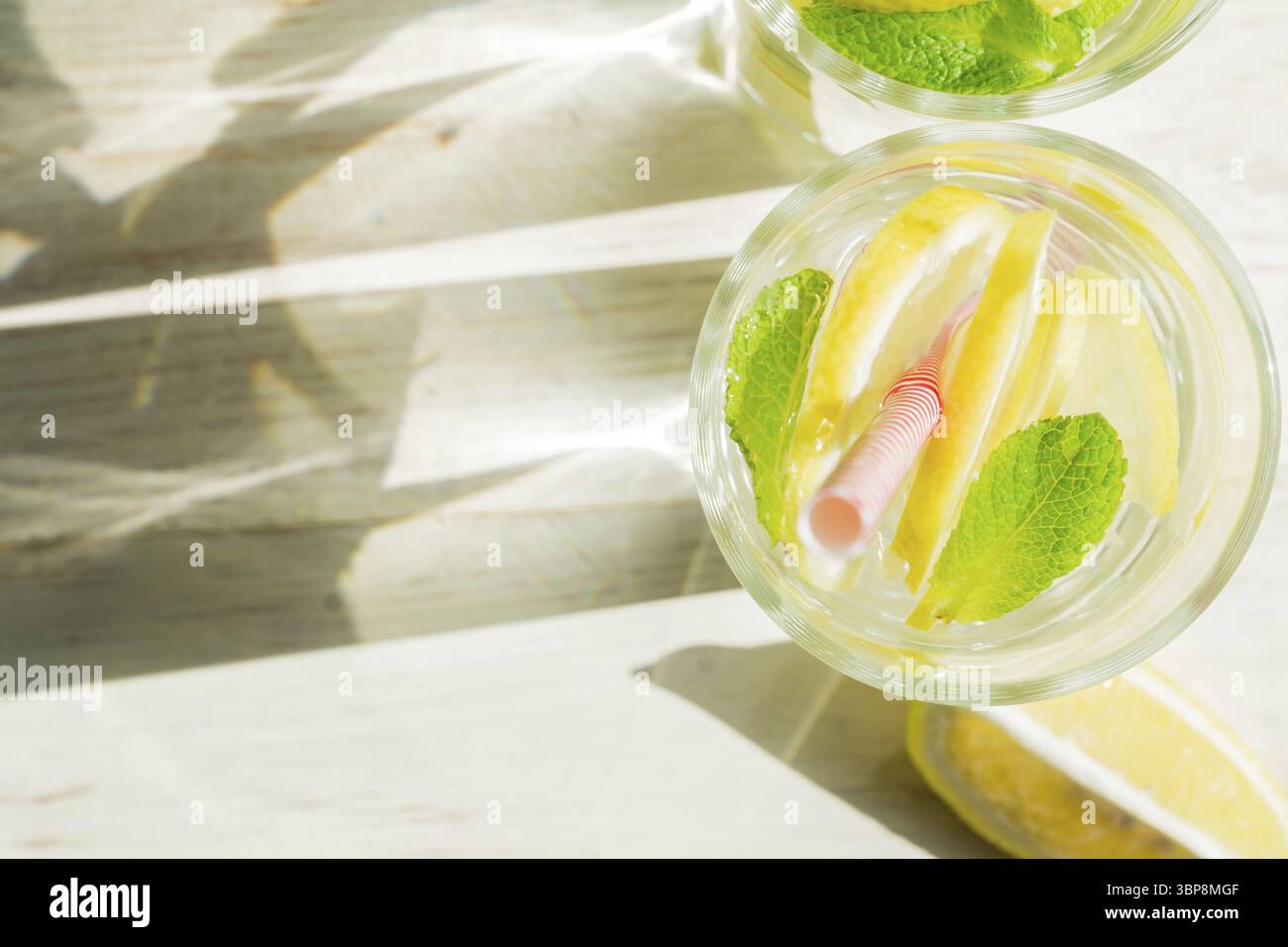 Vista dall'alto del bicchiere di limonata fatta in casa con limoni, menta e cannucce di carta su fondo rustico in legno. Bevanda rinfrescante estiva. ombre dure Foto Stock