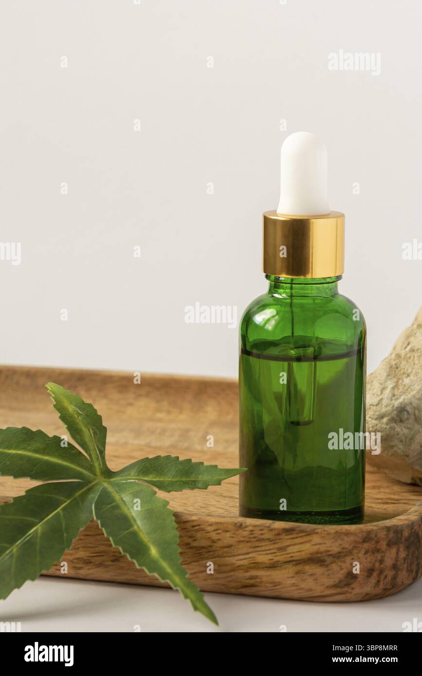 Bottiglia di vetro verde con olio CBD, tintura THC e foglie di canapa su sfondo bianco. stile minimalista. Cosmetici biologici cosmetici con olio CBD Foto Stock