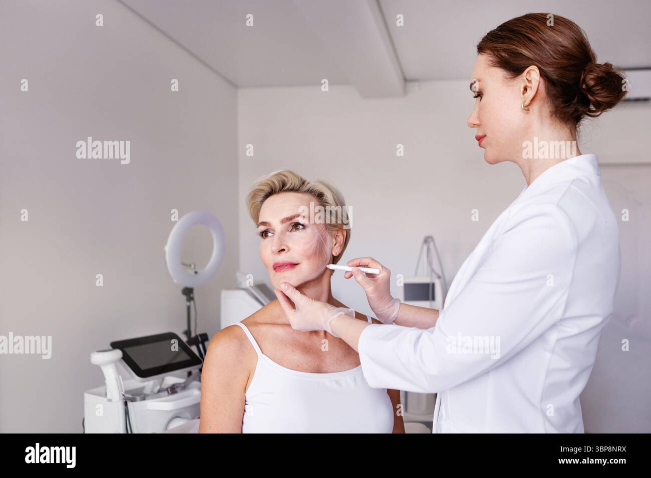 Dermatologo cosmetico che disegna linee di sollevamento del viso su una donna matura in una clinica di bellezza. Consulenza anti-invecchiamento, pianificazione del trattamento estetico, professionismo Foto Stock