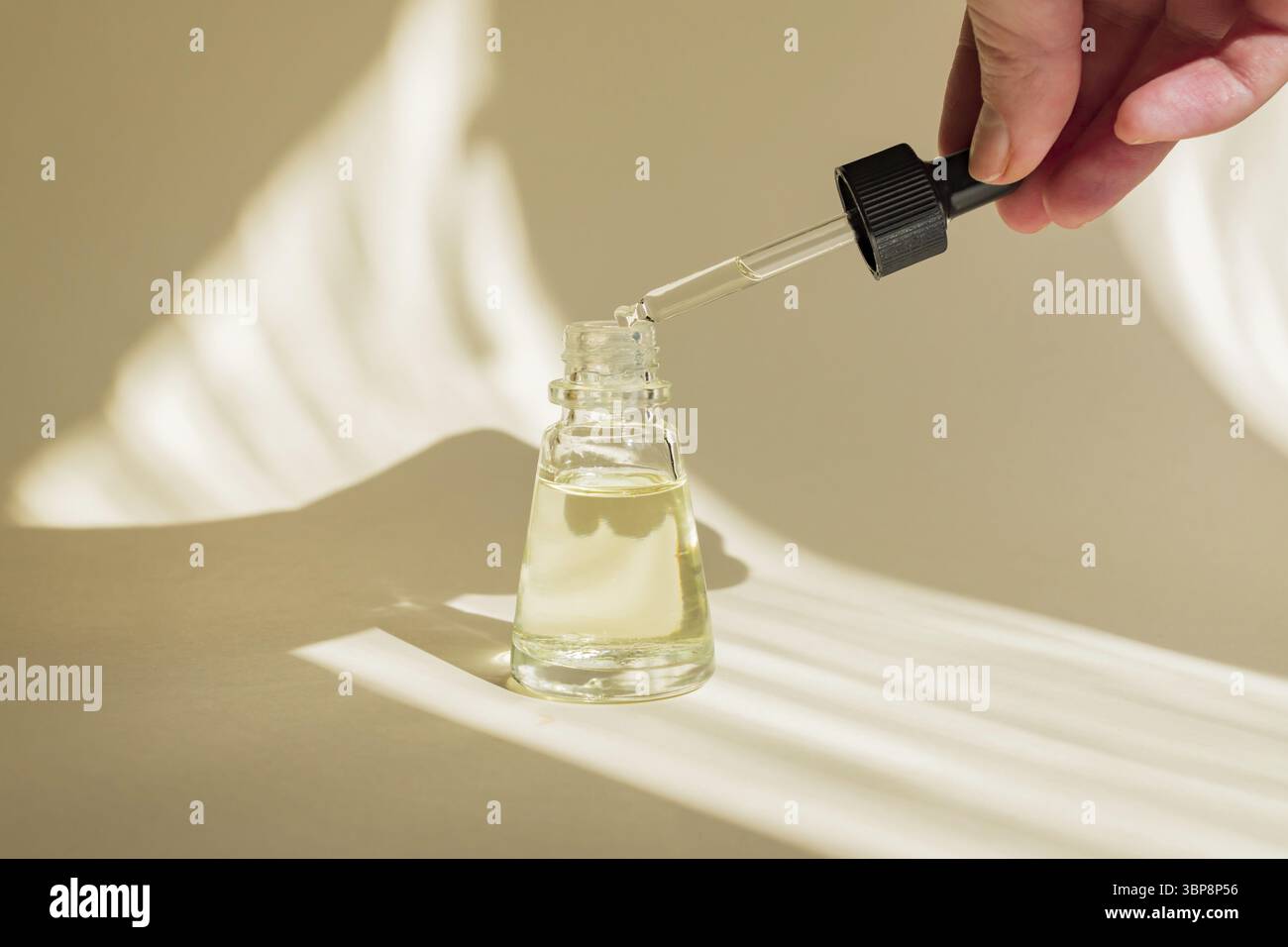 Mano femminile con contagocce di olio essenziale, essenza aromaterapica o liquido medicinale su sfondo beige. Design ombreggiato alla moda Foto Stock