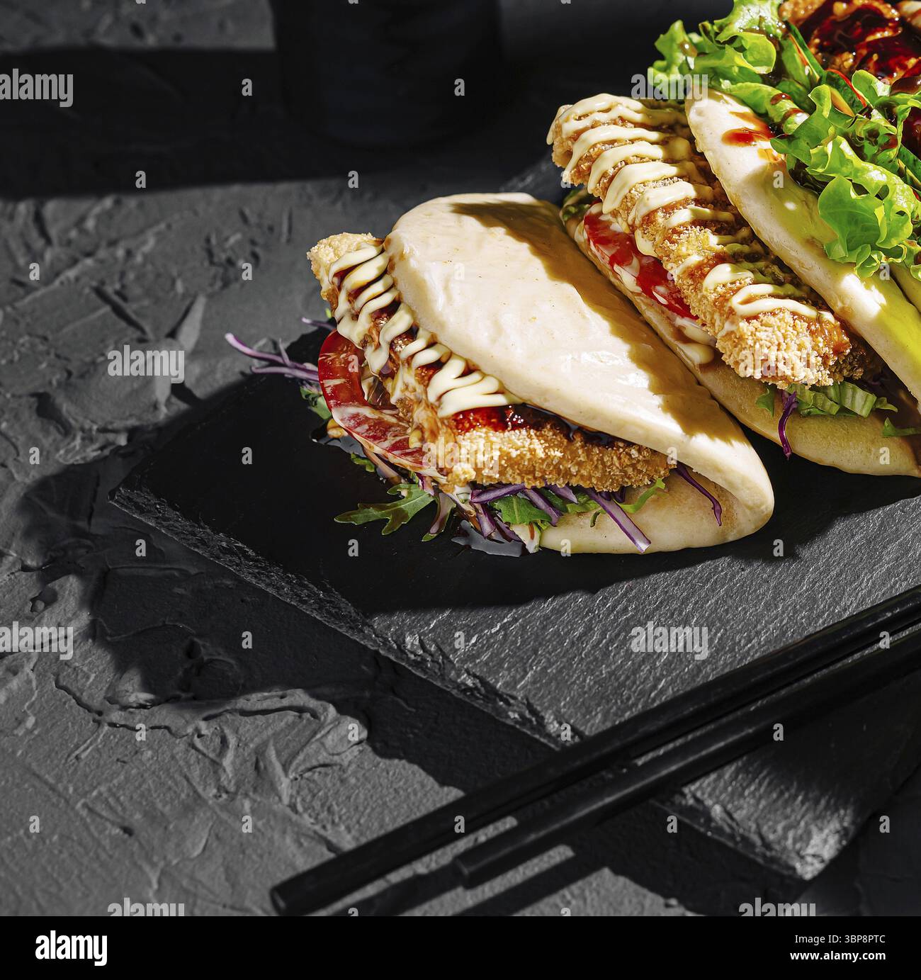 Cibo, due panini bao ripieni di ingredienti fritti croccanti, verdure fresche e salsa sgusciata sono presentati su un piatto di ardesia scura. Una a elegante Foto Stock