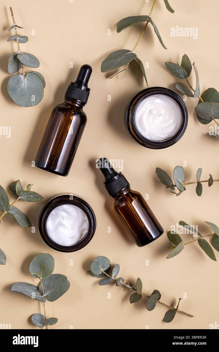 Siero facciale anti-invecchiamento in collagene in flacone di vetro e crema viso su sfondo beige pastello con rami di eucalipto. Bellezza cosmetica organica naturale C. Foto Stock