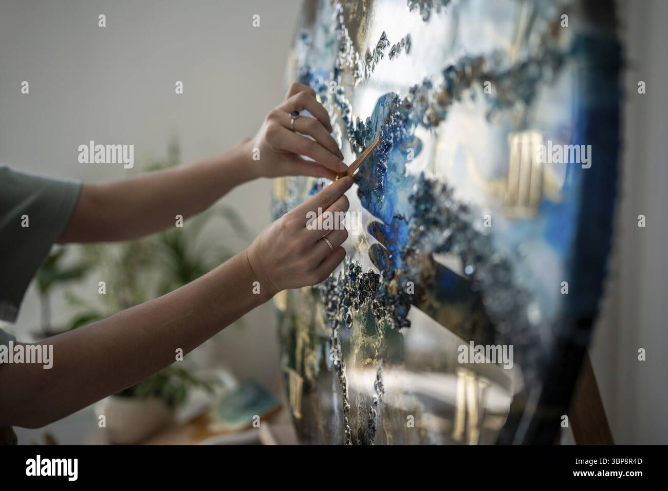 Palme femminili di artista concentrata posizionano le lancette dell'orologio, l'orologio sul prodotto finito in resina epossidica, la pittura. Donna concentrata che prende gli ultimi ritocchi per completare la p Foto Stock