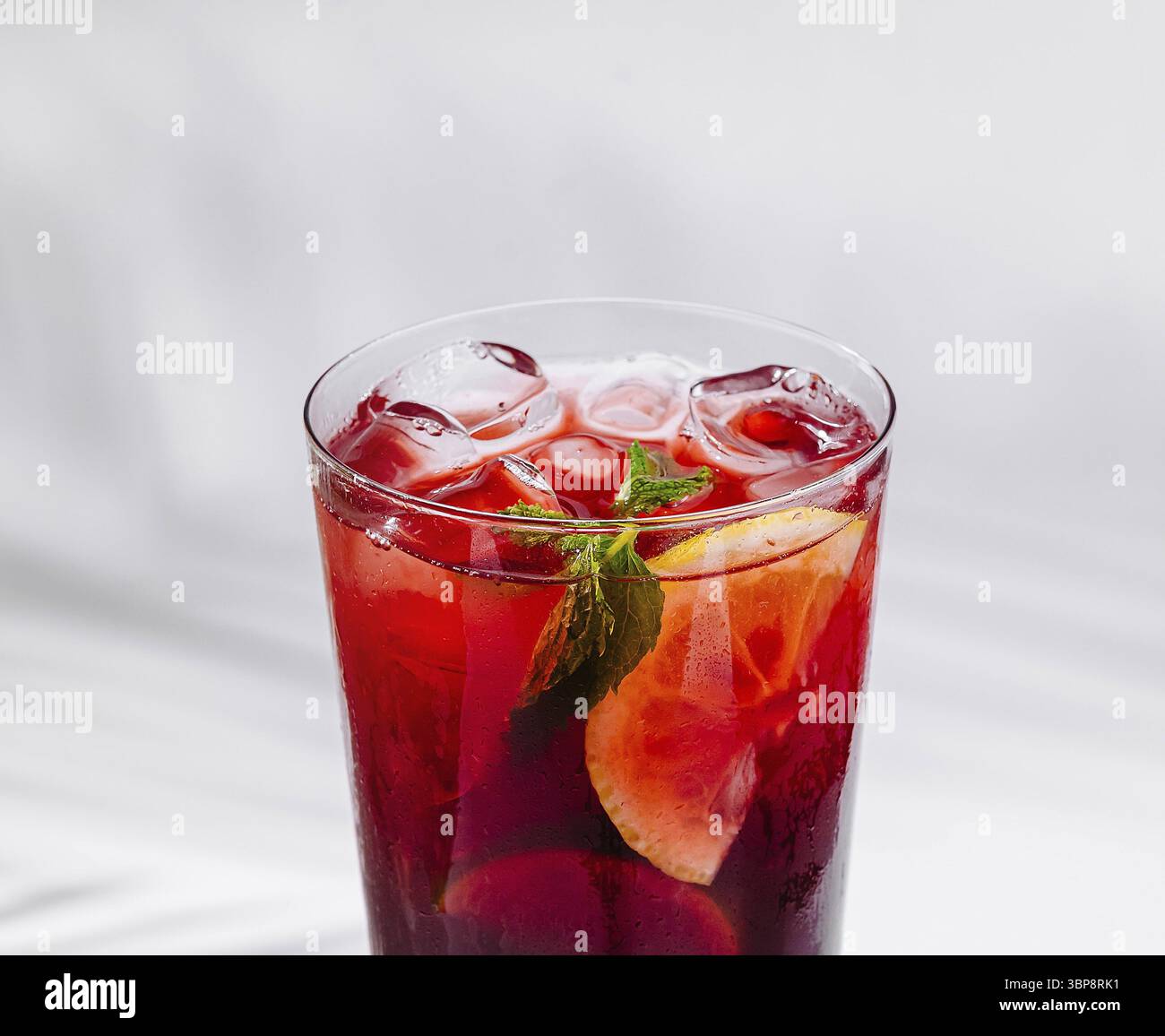 Cibo, cocktail rosso viene versato in un bicchiere con ghiaccio, limone e menta Foto Stock