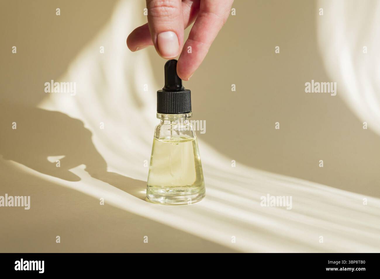 Mano femminile con contagocce di olio essenziale, essenza aromaterapica o liquido medicinale su sfondo beige. Design ombreggiato alla moda Foto Stock