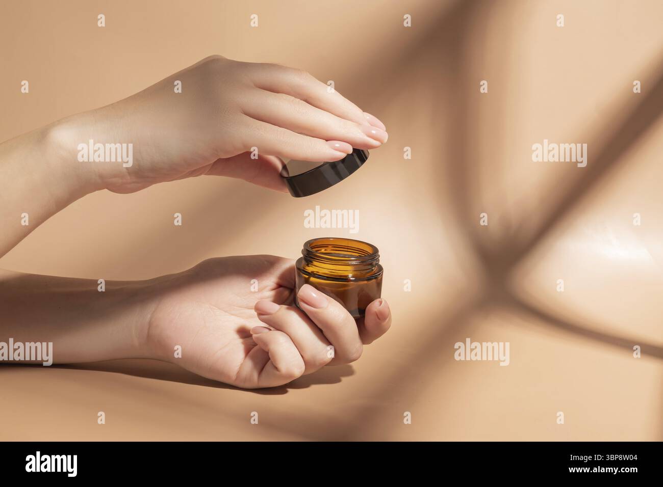 Donna che applica crema sulla mano su sfondo beige con prodotti cosmetici e ombre dure. Concetto di trattamento per la cura della pelle Foto Stock