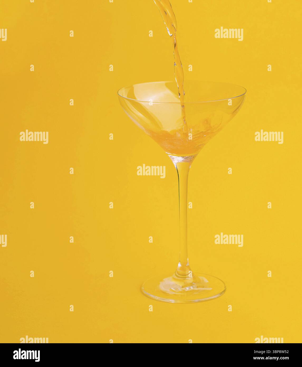 Cibo e bevande rinfrescanti vengono preparate versando succo d'arancia in un bicchiere su un vibrante sfondo giallo Foto Stock