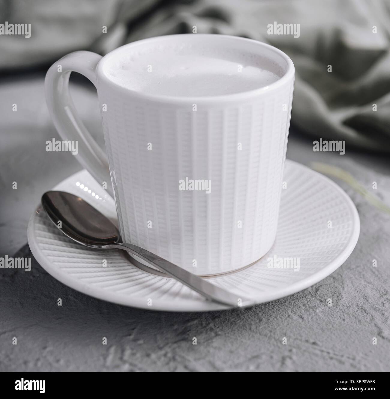 Potrai gustare un'accogliente mattina con un cappuccino a base di latte in una tazza bianca semplice ed elegante su un tavolo strutturato circondato da foglie verdi, creando così Foto Stock