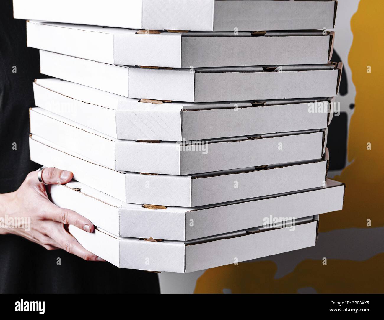Cibo: Una persona tiene una pila alta di scatole bianche per pizza, mostrando una serie di contenitori da asporto. Lo sfondo presenta un design contemporaneo, oltre ad Foto Stock