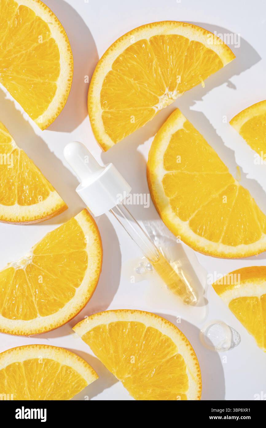 Primo piano della pipetta con il versamento di siero liquido e ombre sullo sfondo delle arance. Cosmetici alla moda con ombre dure Foto Stock