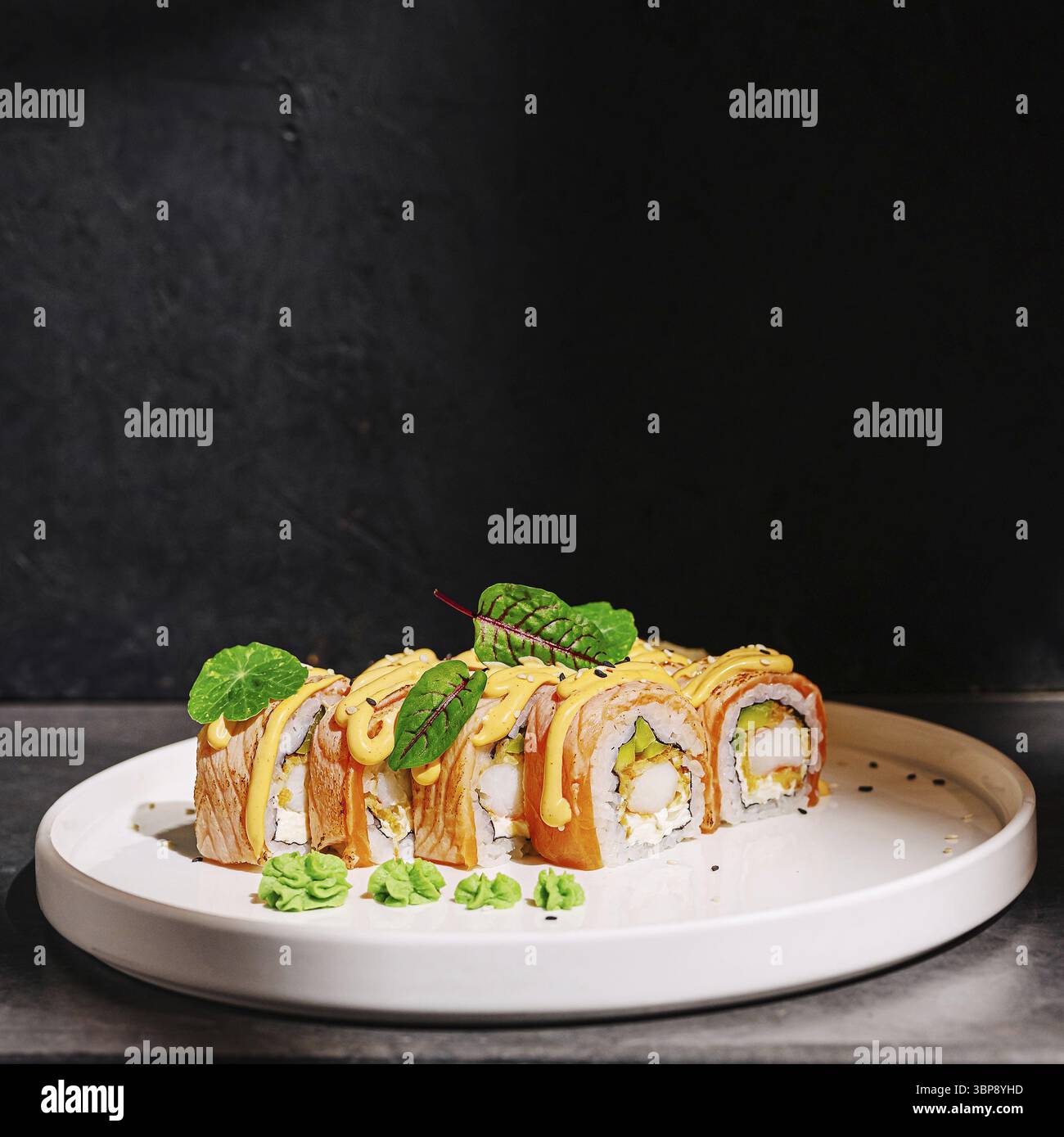 Cibo, Un vivace sushi roll con strati di pesce, riso e verdure è presentato su un elegante piatto bianco. I wasabi freschi e i verdi aggiungono colore al loro colore Foto Stock