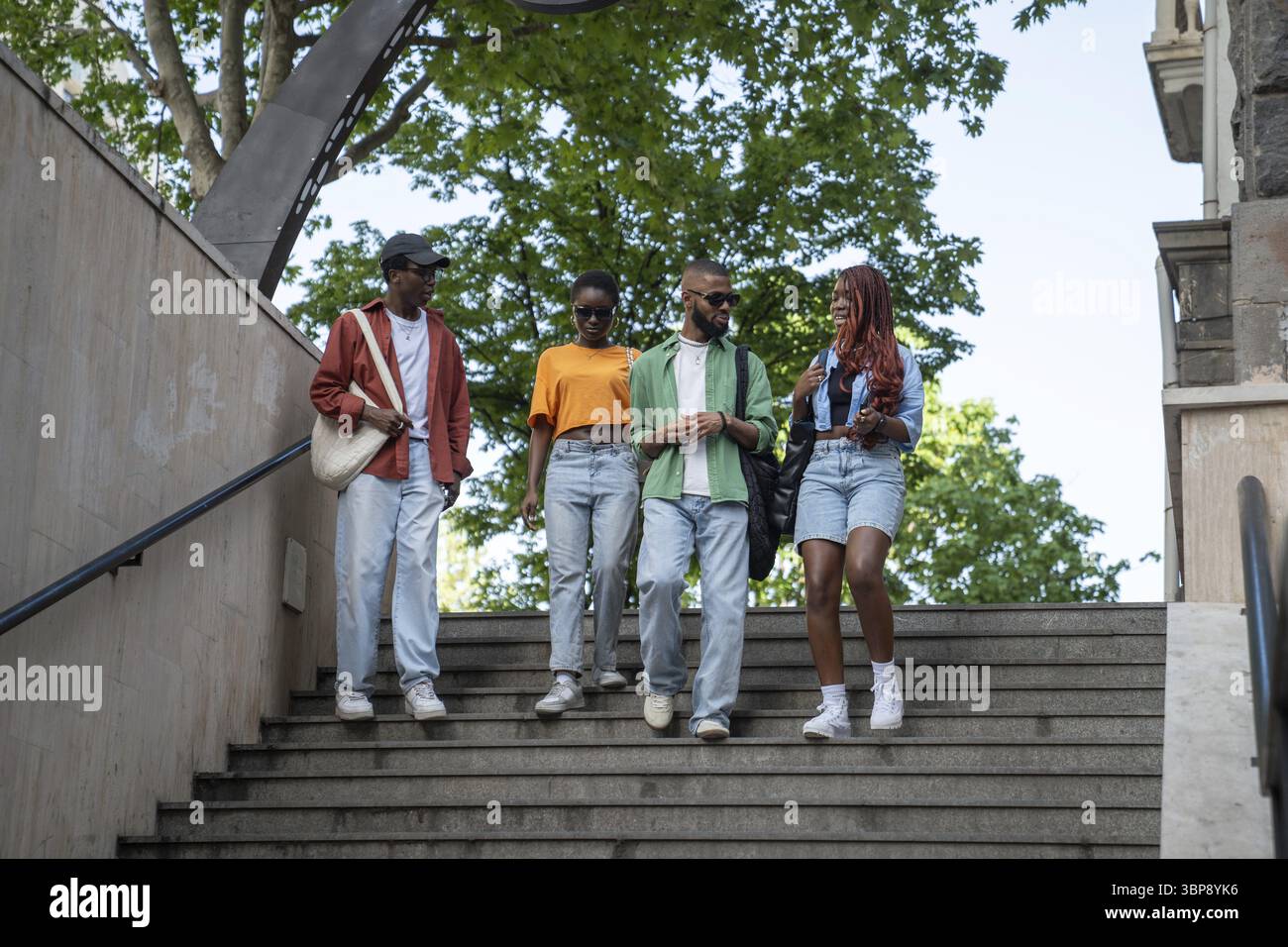 Un gruppo di eleganti amici afroamericani passeggia per le strade della città, entra nel sottopassaggio e trascorri del tempo con conversazioni emozionanti. Studenti neri seri Foto Stock