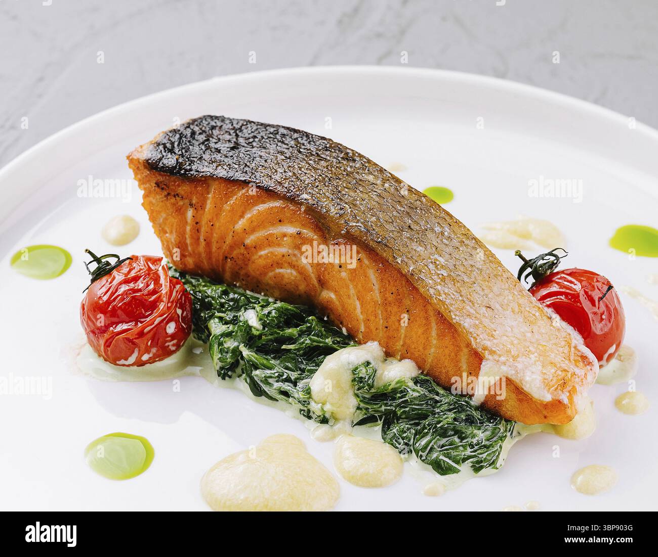 Cibo, presentazione elegante del salmone alla griglia su un letto di spinaci con pomodori ciliegini arrostiti Foto Stock