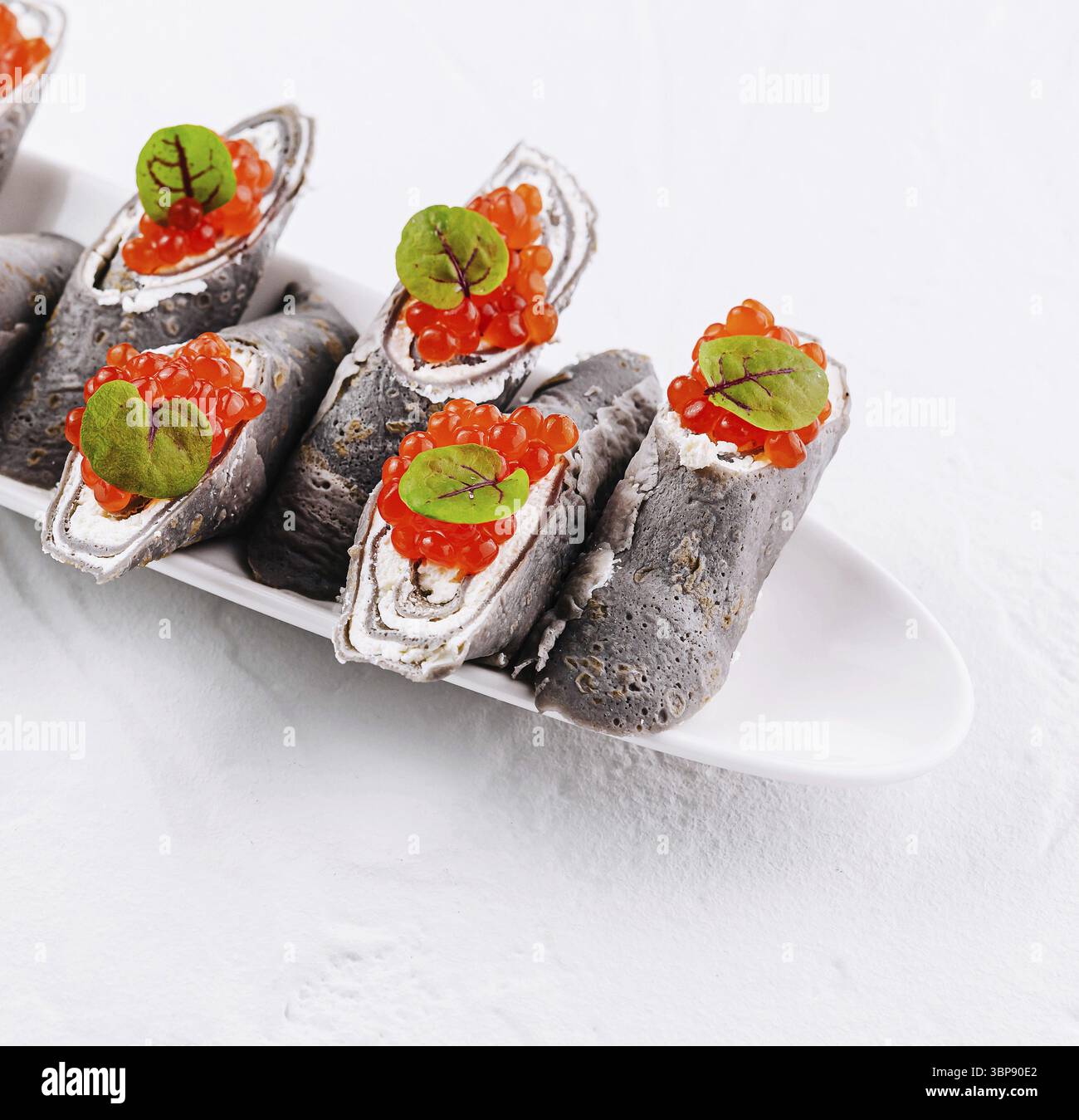 Cibo, eleganti panini crespati neri ripieni di formaggio spalmabile e ricoperti di caviale rosso ed erbe fresche Foto Stock