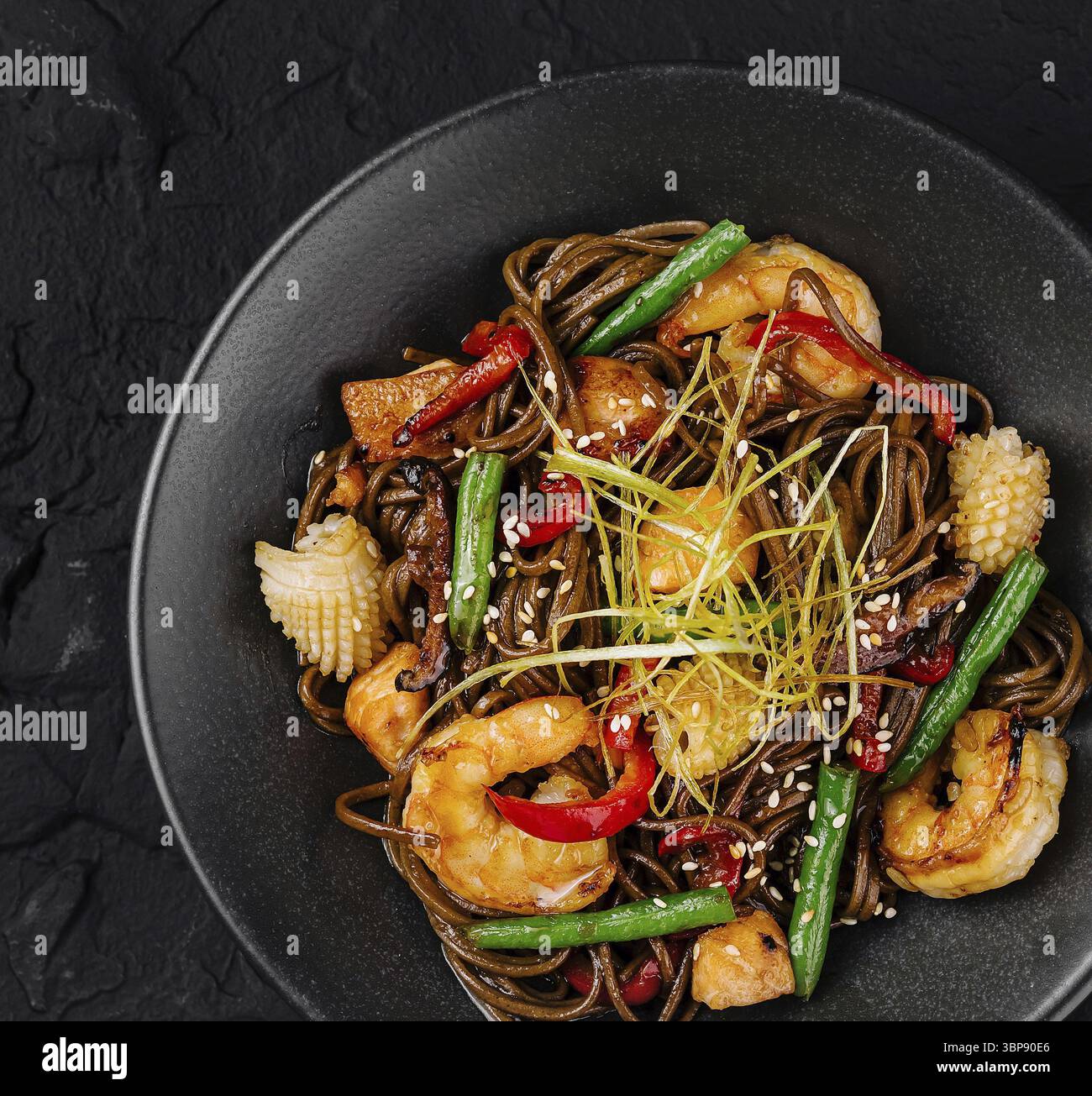 Cibo, cucina asiatica: Spaghetti saltati in padella con gamberi, verdure e guarnire in una ciotola nera su uno sfondo scuro Foto Stock